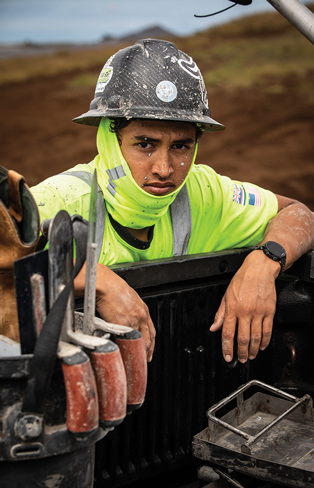construction worker in hard hat looking towards you leaning on truck bed. 